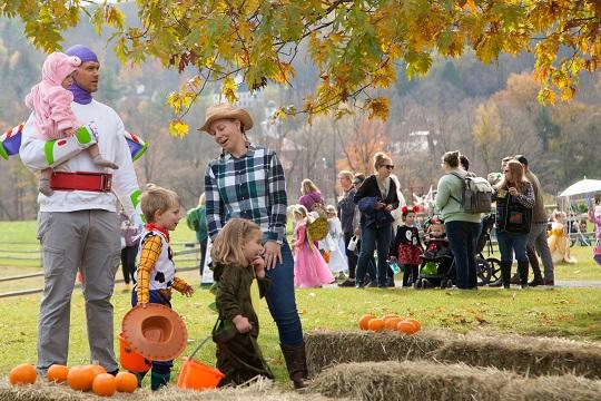 Families with kids dressed in costumes on a lawn with hay bales.