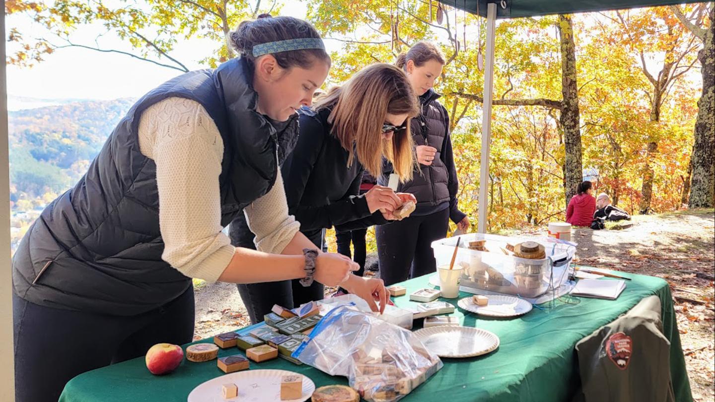 Three people in hiking attire do an arts and crafts activity with tree cookies