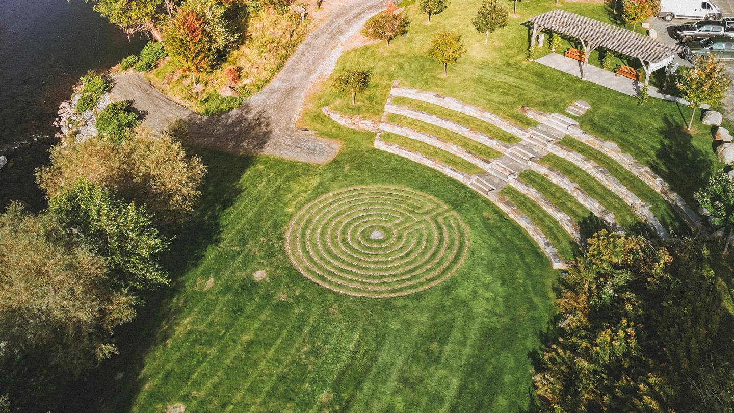 Drone image of east end park with grassy lawn, amphitheater seating, and pergola alongside the river