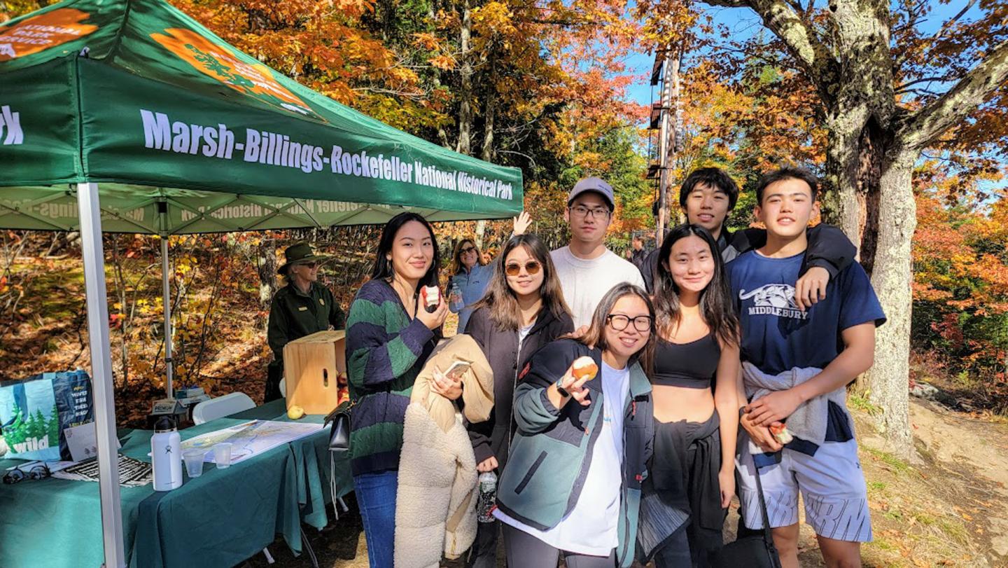 Group of seven young adults pose in front of tent that reads "Marsh-Billings-Rockefeller National Historical Park"