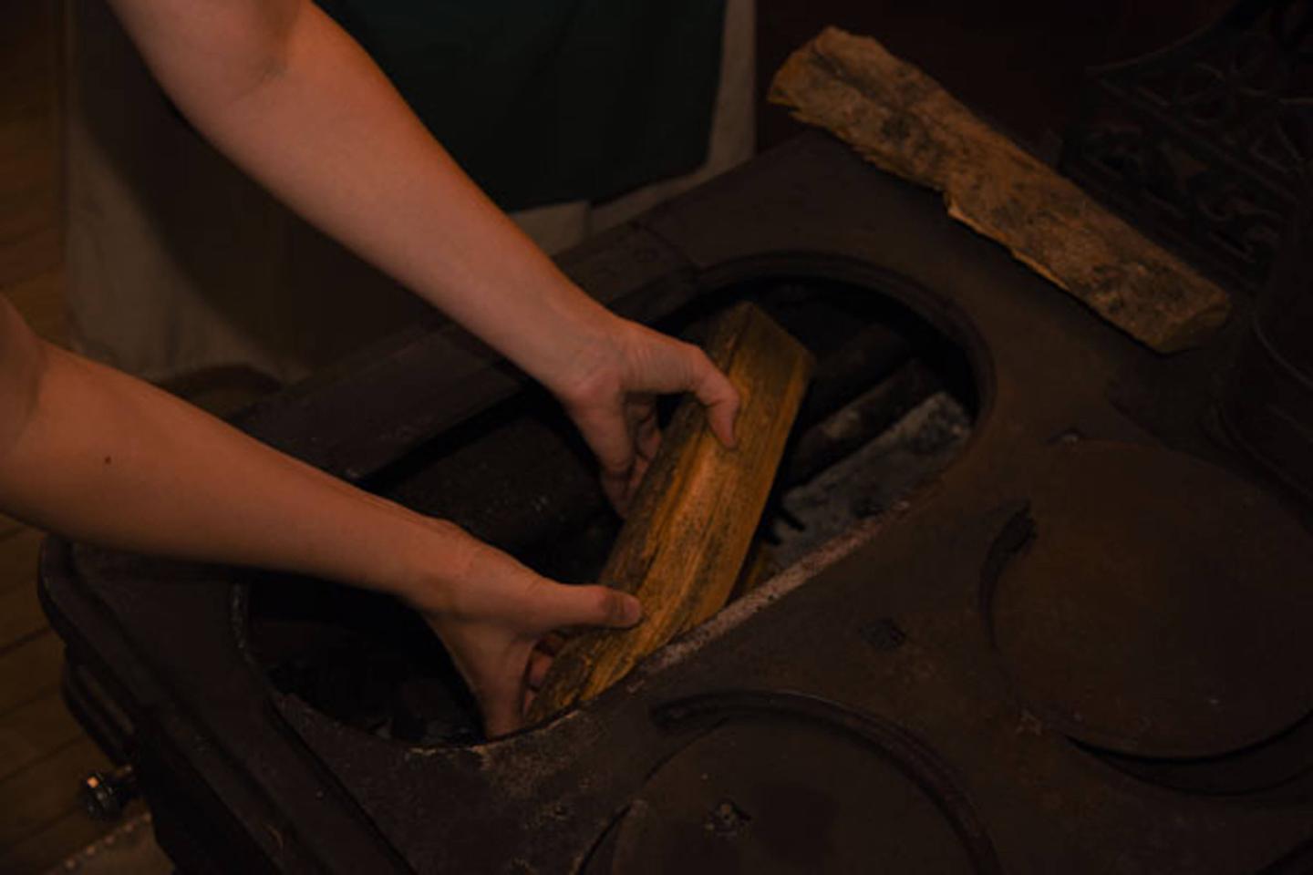 Putting firewood in chamber to heat stove.
