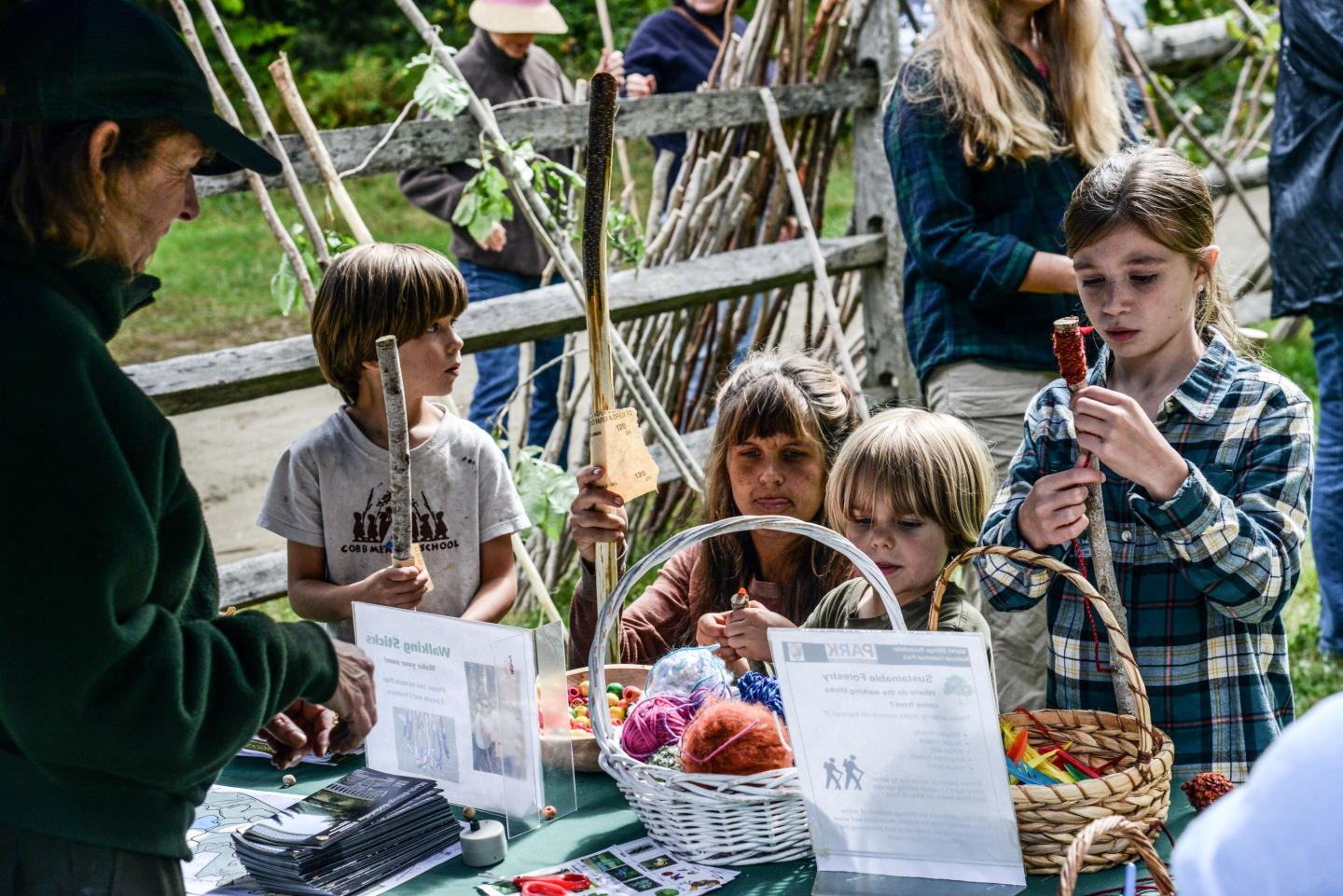 three children and one adult are assisted by a park ranger as they decorate walking sticks with yarn