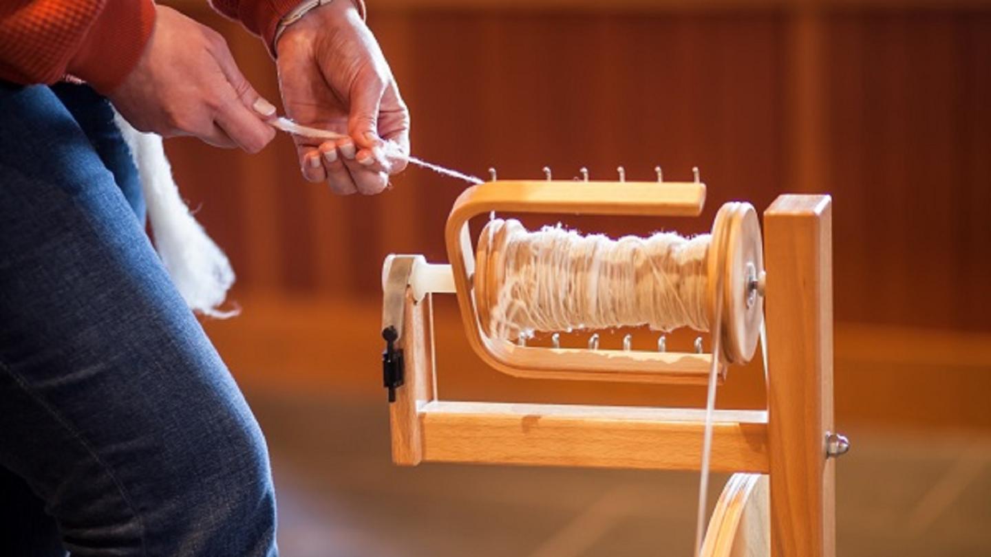 Hands holding wool as it is being made into yarn on a spindle.