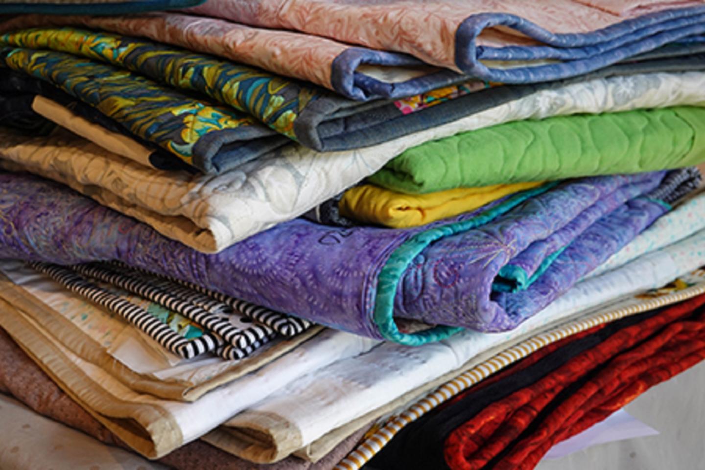 Colorful folded quilts in a pile.