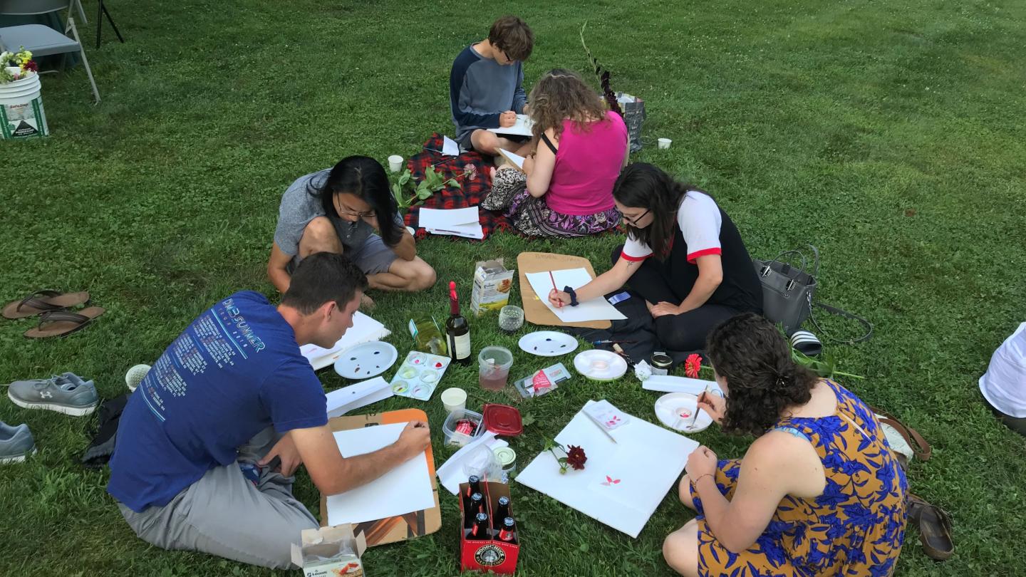 Group of 6 people sit on lawn concentrating on watercolor paintings
