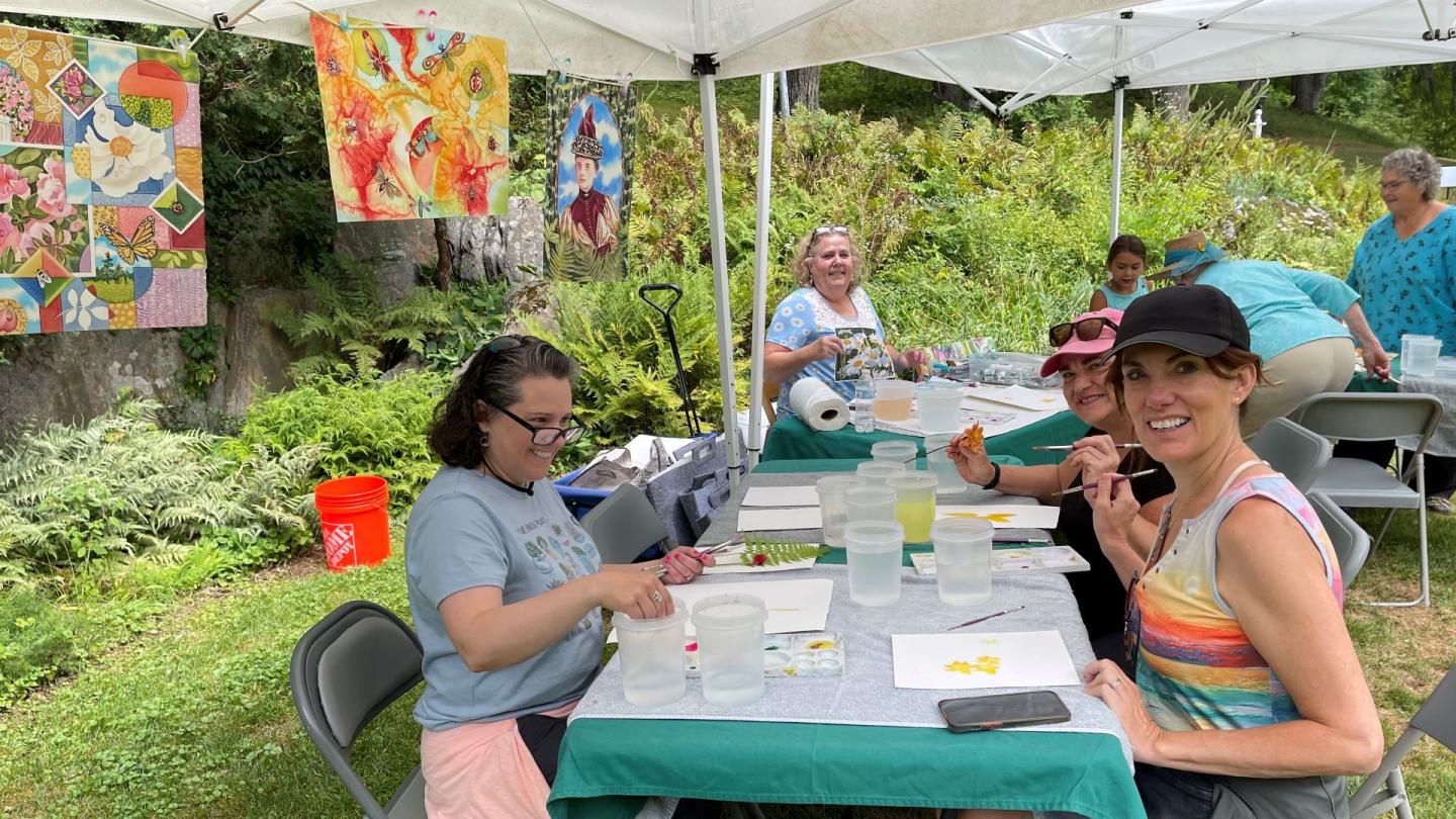 Group of 3 sits at table and paints watercolor flowers