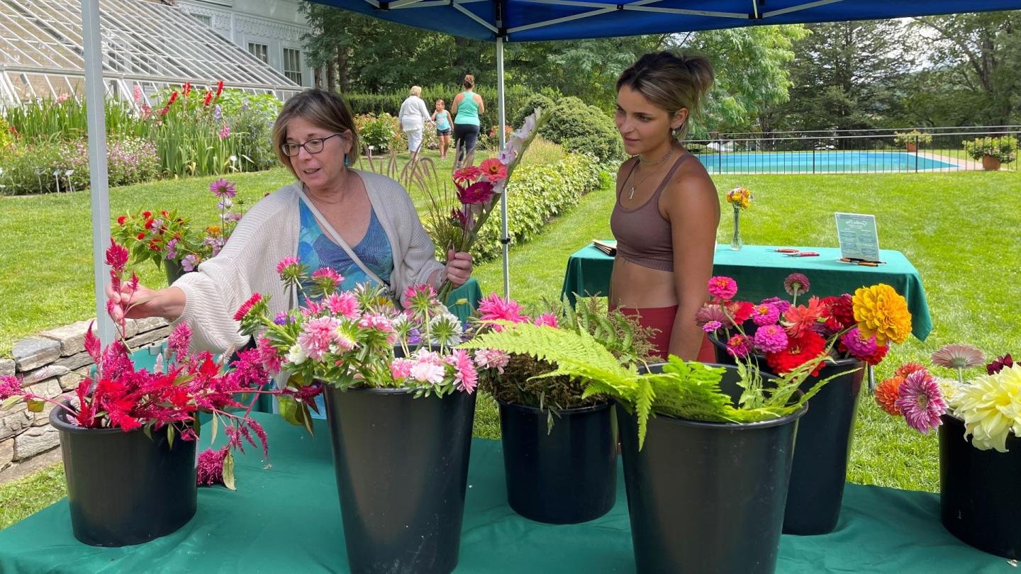 Two people create flower bouquets surrounded by buckets of fresh flowers