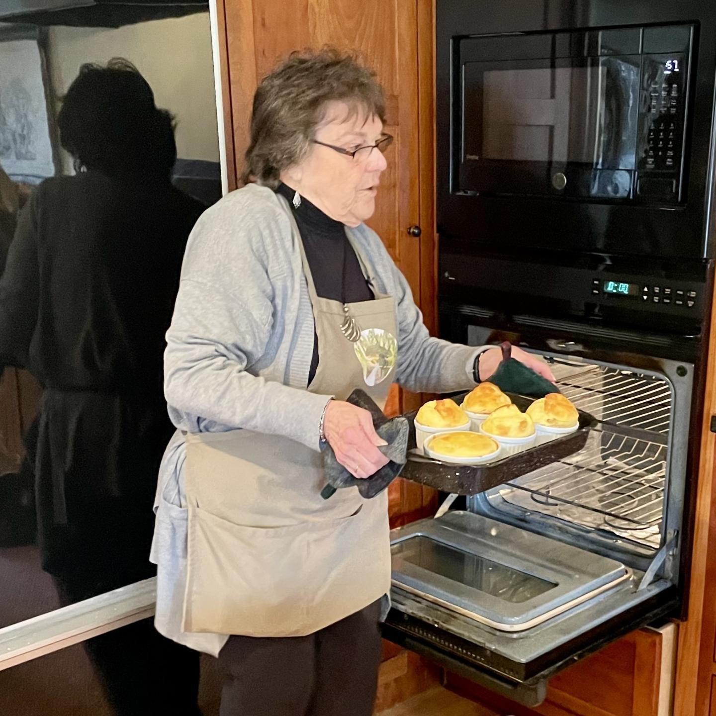 Woman carrying a pan of small soufflés just out of the open oven