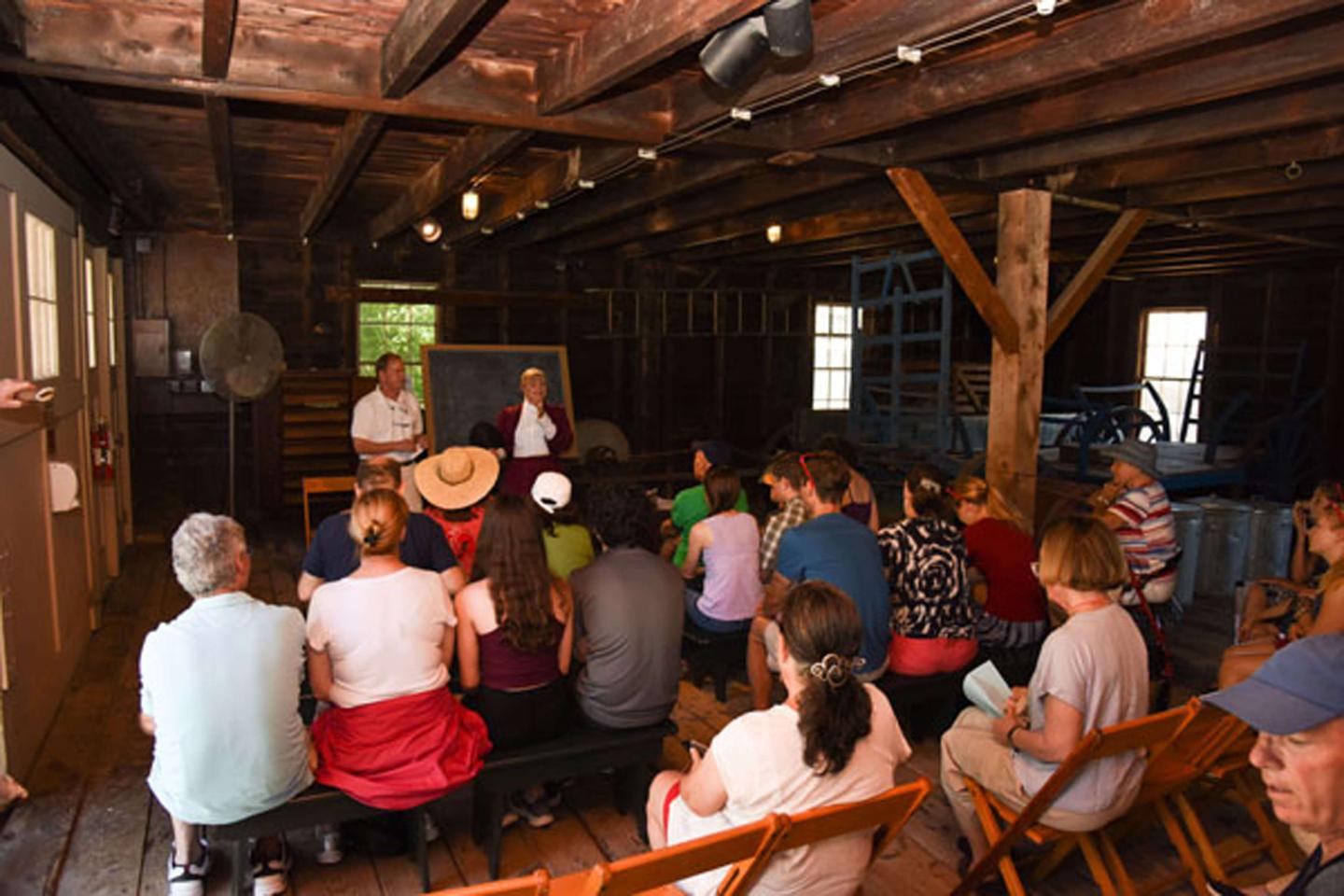 Guests watching a lecture or debate in an old schoolhouse setting.