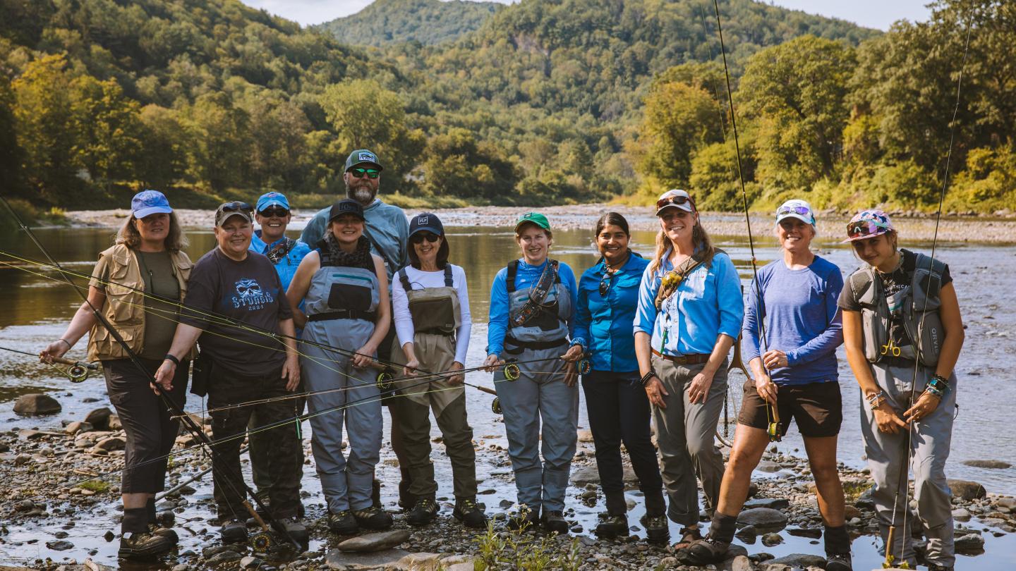 Group of women holding fly fishing gear while standing on a riverbank