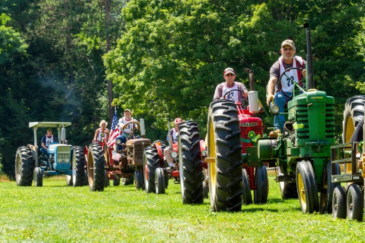 A parade of tractors on green grass.  