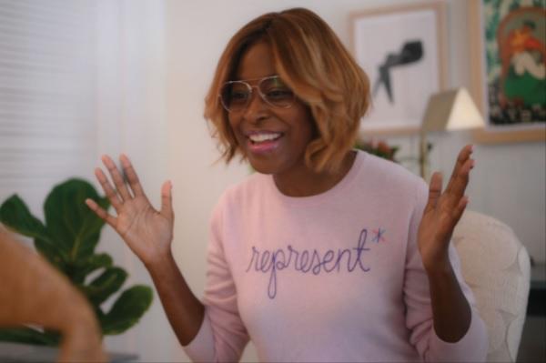 Person in a pink sweater wearing glasses smiling with their hands open and ready to clap.