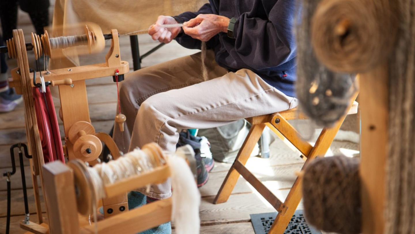 A person making yarn from fleece on a wooden spinning machine.