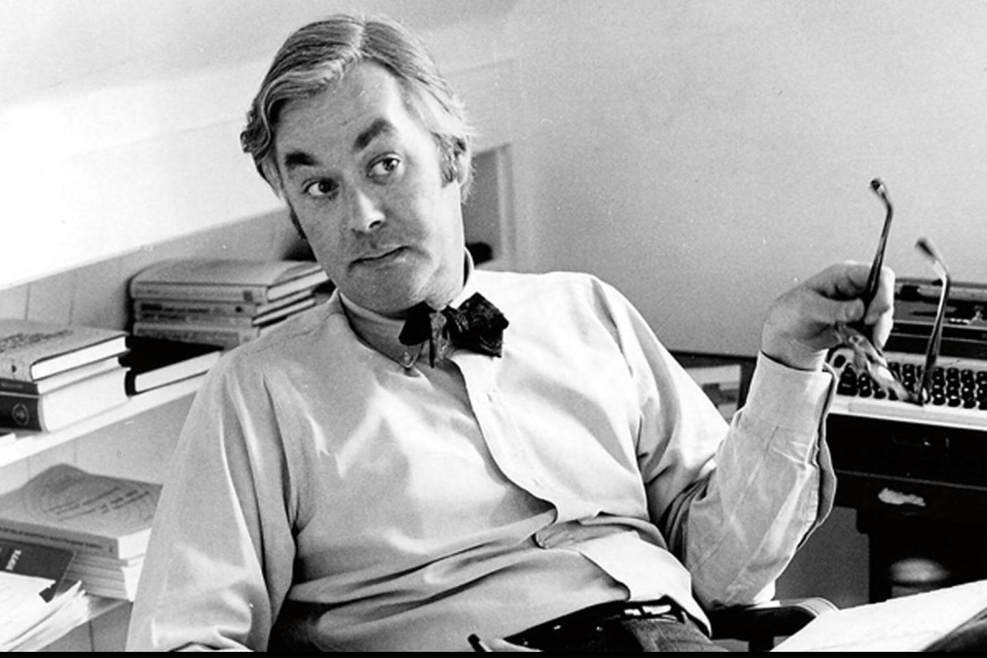 Daniel Patrick Moynihan sits in a chair in his office with his glasses in hand