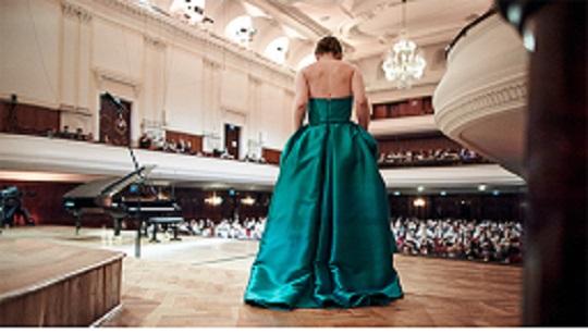 Female in a teal colored dress with her back to the viewer on stage in front of an audience.