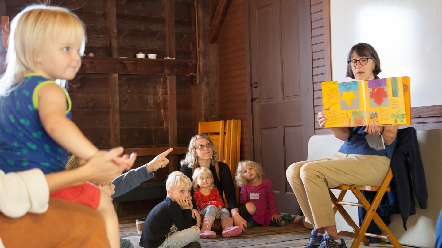 Children listening to a story being read by an adult sitting in a chair.