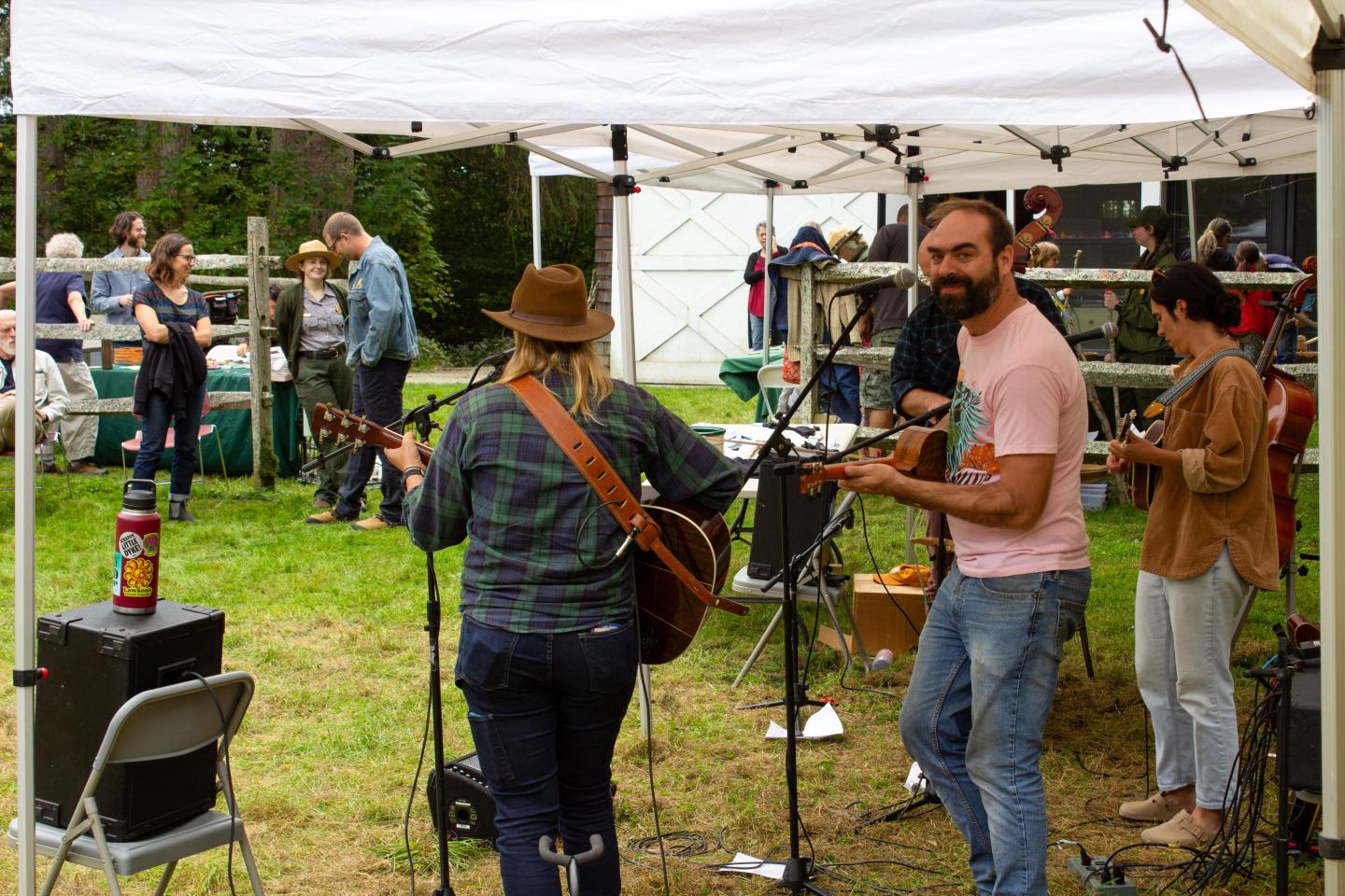 4 piece string band plays music under a tent while crowd watches in a field