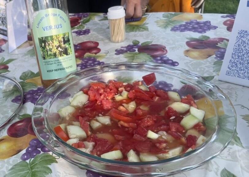 a bottle of verjus next to a bowl of cucumber and tomatoes marinating in said verjus