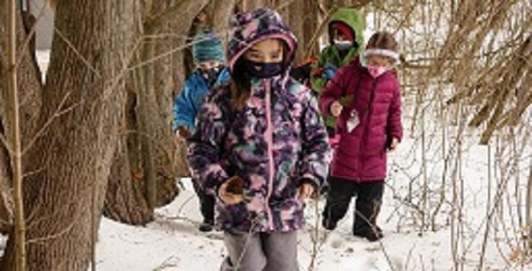 Kids walking in the winter woods with snow on the ground.