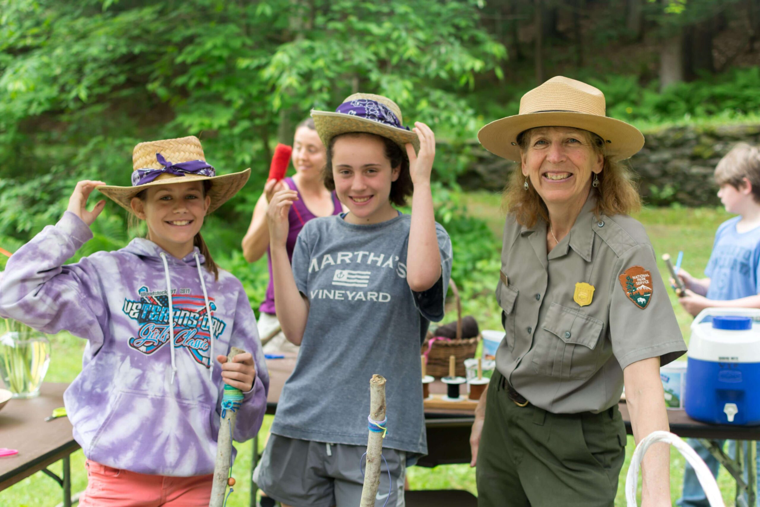 Two young girls stand next to a National Park Service ranger with walking sticks in hand.