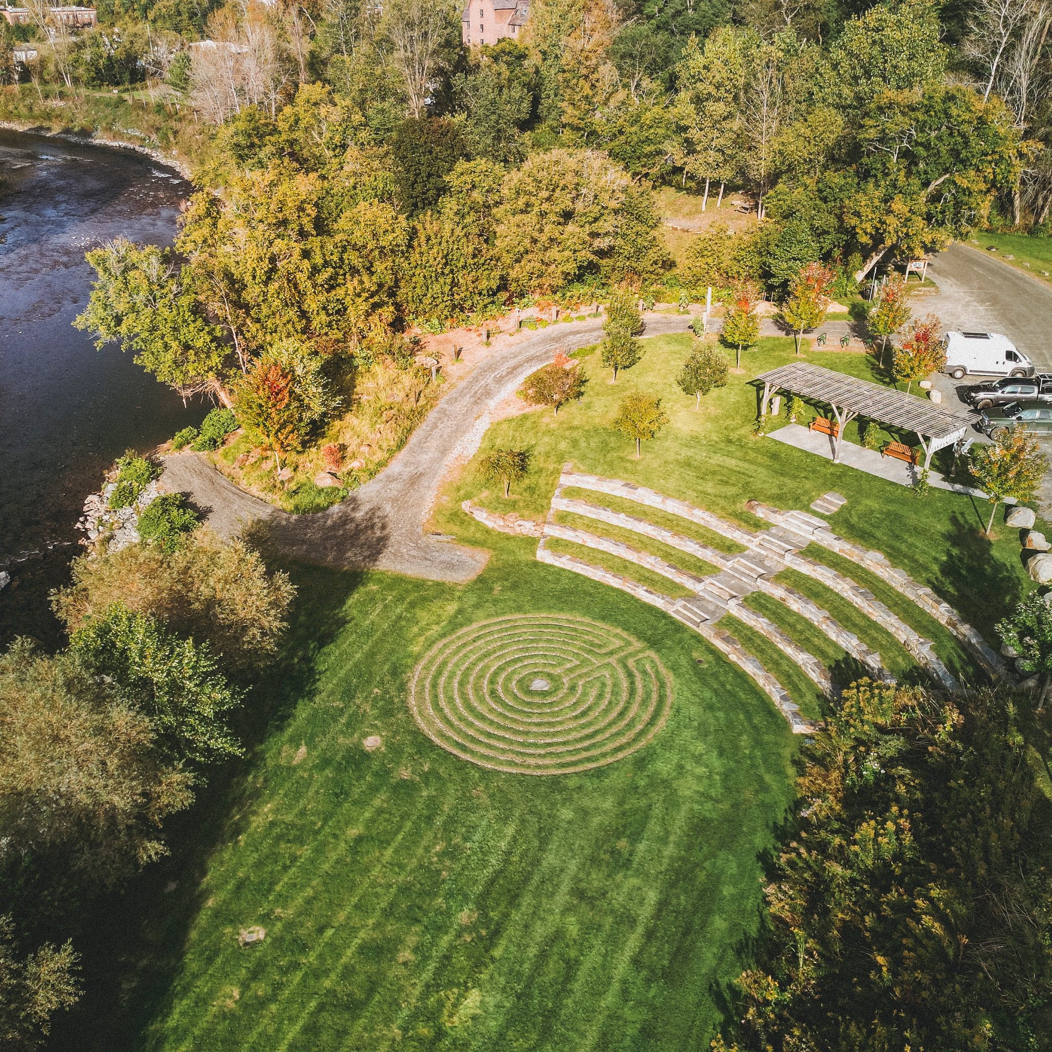 Drone image of east end park with grassy lawn, amphitheater seating, and pergola alongside the river