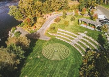 Drone image of east end park with grassy lawn, amphitheater seating, and pergola alongside the river