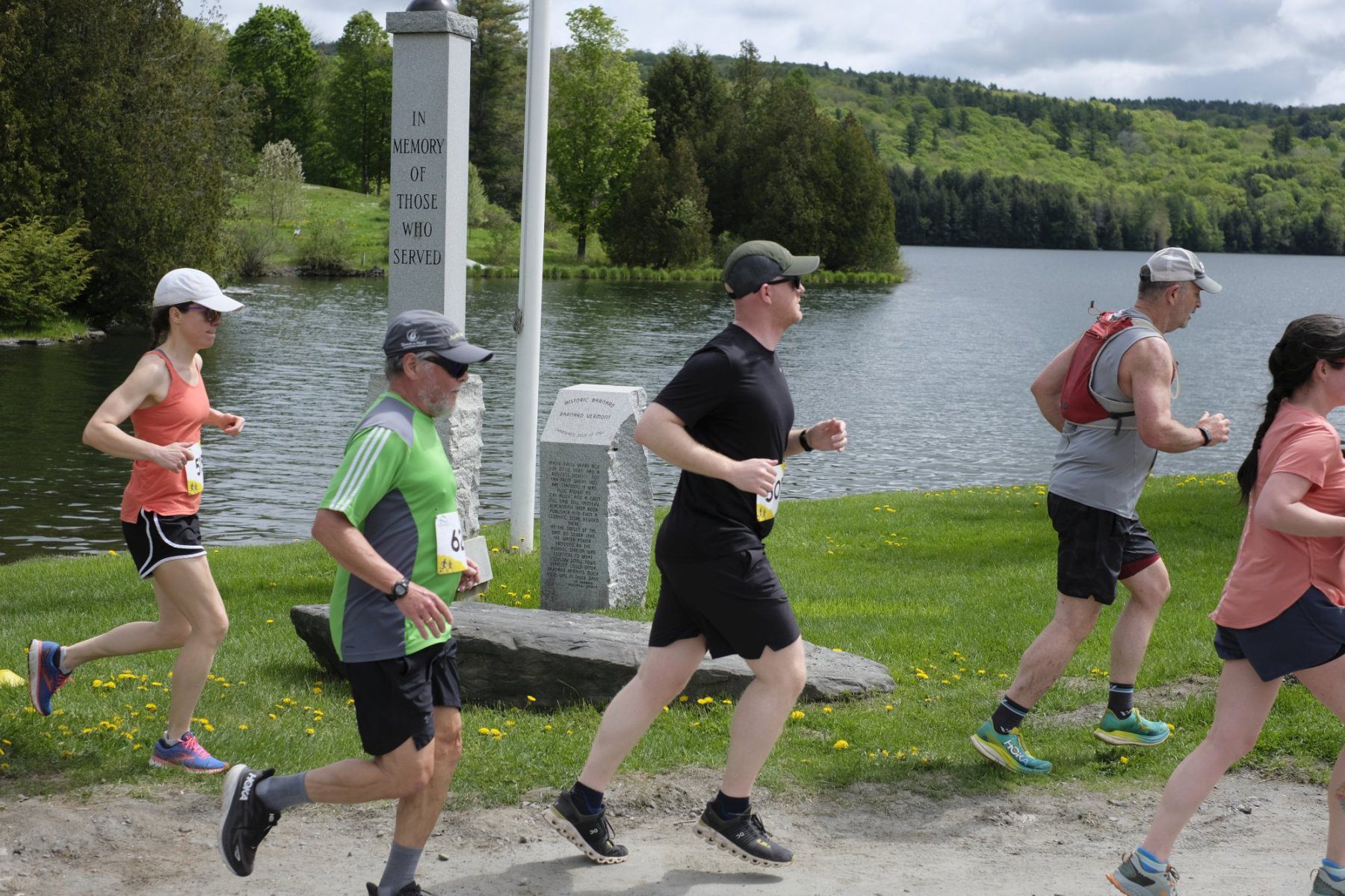 Five people run past a lake on a spring day.