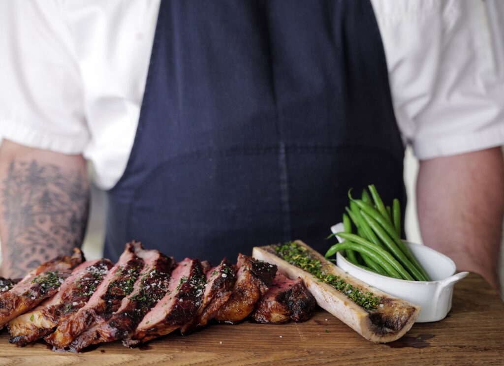 A chef holding a tray of steak